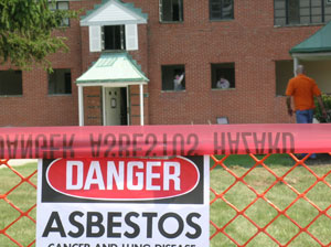 danger asbestos sign on a fence in front of an old, brick building